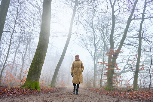 Woman in white coat walking on remote countryside rural road on cold freezing foggy day. Winter weather.