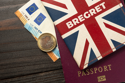 Bregret (Brexit regret) concept: a leather wallet over a passport and some euros on a wooden table