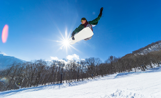 A Japanese snowboard rider does a jump on a sunny day with the sun behind him.