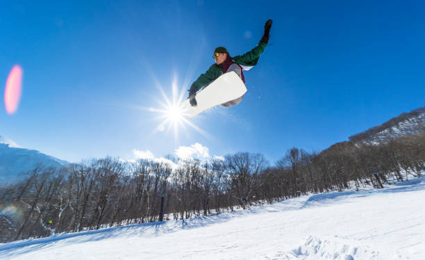 Snowboarder doing a jump on a sunny day A Japanese snowboard rider does a jump on a sunny day with the sun behind him. japanese snowboarder stock pictures, royalty-free photos & images