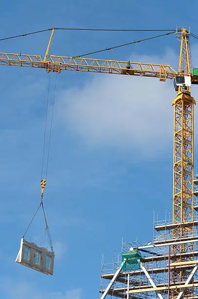 A towercrane is hoisting a facade element on the construction site of a high-rise building