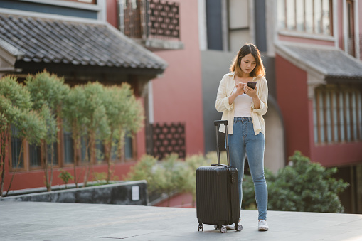 Young Asian woman solo traveler with suitcase using phone gps while worried journey on the trip. Urban transportation and travel concept.