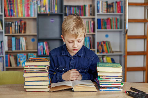 Child boy reads book from bookshelves in library. Bookstore concept, education and knowledge. World Book Day