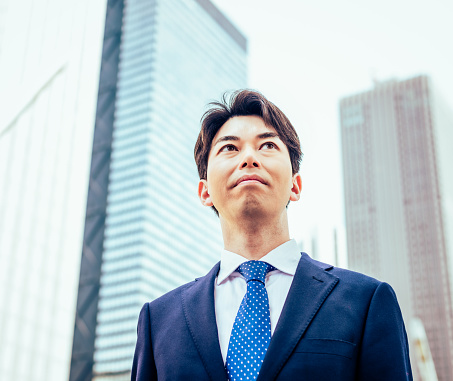 A confident businessman looking up at office towers on the skyline in Ginza, Tokyo.