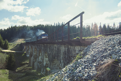 Train passing railway bridge near Carpathian forest landscape photo. Old railroad in mountains. Nature scenery photography. Ambient light. High quality picture for wallpaper, travel blog, magazine