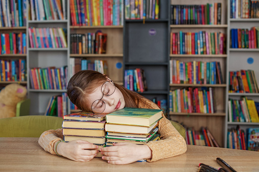 Child girl reads book from bookshelves in library. Bookstore concept, education and knowledge. World Book Day