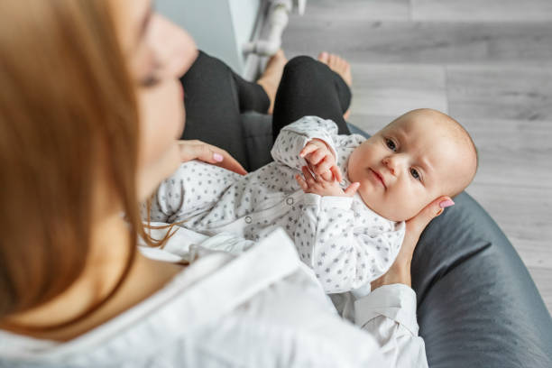 la mère s’occupe du nouveau-né à la maison. maman tient sa petite fille de deux mois dans ses bras. - patient male nurse nurse hospital photos et images de collection