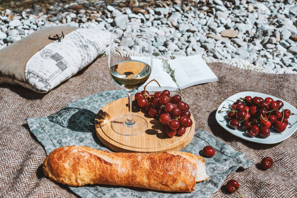 istock Summer romantic rustic picnic on the beach, white wine glass, baguette, cherries, grape and open book 1470921085