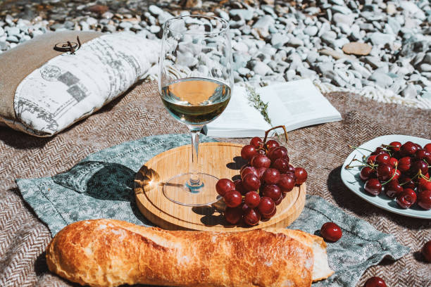 istock Summer romantic rustic picnic on the beach, white wine glass, baguette, cherries, grape and open book 1470921087
