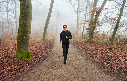 Mid adult woman in forest jogging on forest path