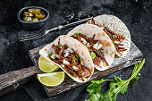 Pork carnitas tacos on corn tortillas with onion and lime. Black background. Top view