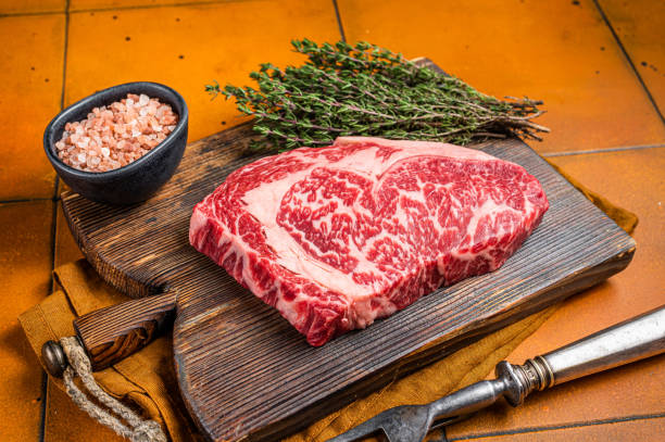 Prime Raw wagyu Rib Eye beef meat steak on wooden board. Orange background. Top view Prime Raw wagyu Rib Eye beef meat steak on wooden board. Orange background. Top view. wagyu beef stock pictures, royalty-free photos & images