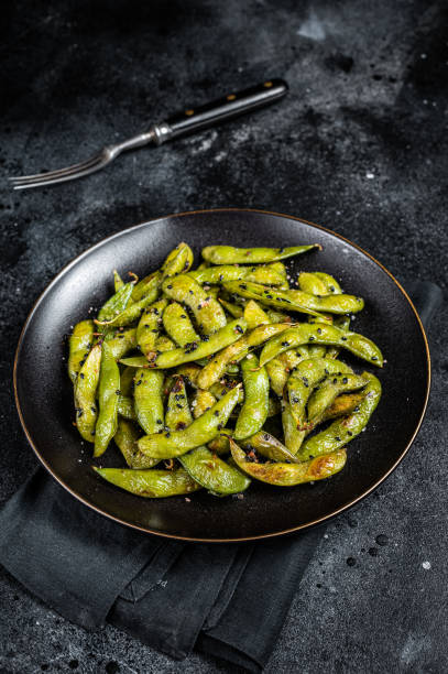 Stir-fried green Edamame Soy Beans with sea salt and sesame seeds in a plate. Black background. Top view