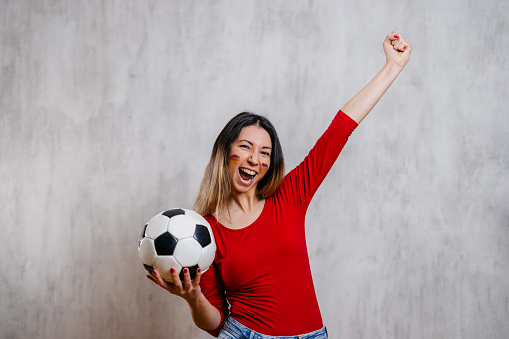 Portrait of a beautiful young woman with painted German flag colors on her cheeks, holding a soccer ball.