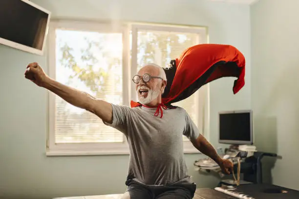 Cheerful mature man having fun while pretending to be a superhero at doctor's office.