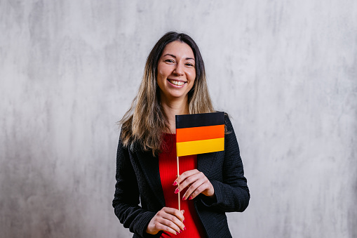 Portrait of a beautiful young woman indoors, holding up a German flag pennant.