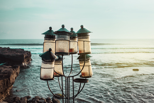 A outside lamps, lanterns in the candlestick with candles on the ocean and cliffs background. Romantic sunset on the sea coast. Bali, Indonesia. Echo beach. Canggu.