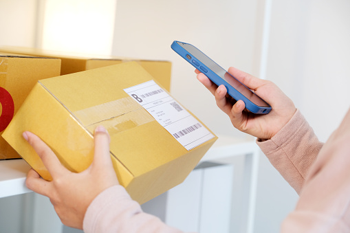 Close up of woman hand holding mobile phone and scanning product box for delivering to customer, online shopping, small business