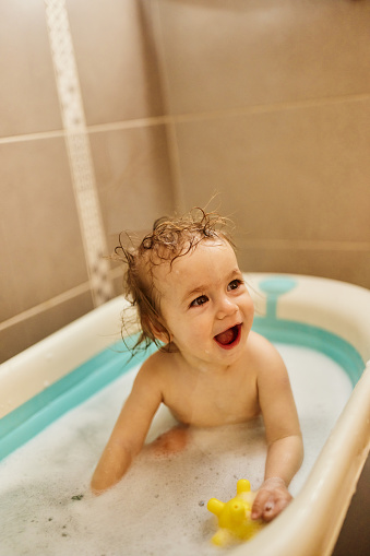 Cute little baby girl having fun in bath tube at home