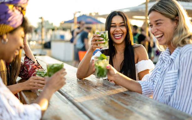 Young women celebrating at beach chiringuito, focus on brunette woman with toothy smile Young women celebrating at beach chiringuito, focus on brunette woman with toothy smile bar exterior stock pictures, royalty-free photos & images