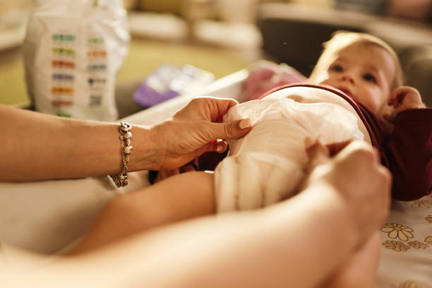 Mother changing her baby girl’s diaper on the bed at home