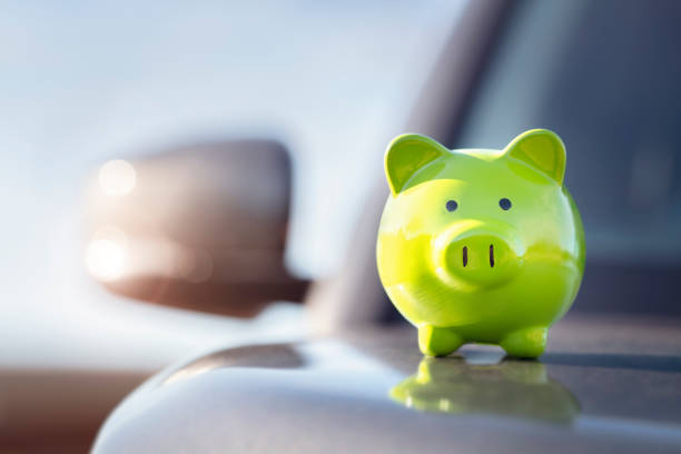 Green piggy bank money box on top of car hood, new vehicle purchase, insurance or driving and motoring cost stock photo