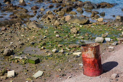 Barrel and waste on a coastline (pollution concept).