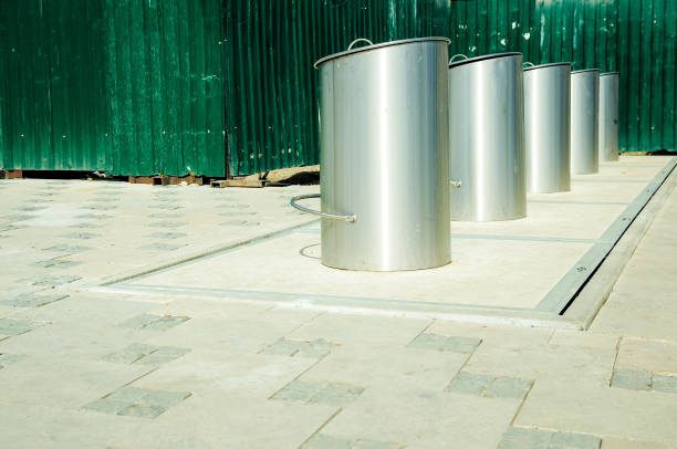 Shiny metal garbage can by the green fence.
