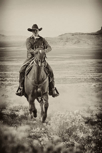 Cowboy on Horseback A man wearing old western attire rides a horse across a country plain. Vertical shot. horseback riding photos stock pictures, royalty-free photos & images