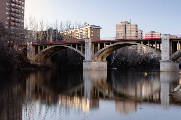 Low point of view at water level on one of the banks of the Pisuerga river as it passes through Valladolid-Spain. Concrete bridge with two big arches. On the opposite bank you can see tall residential buildings.