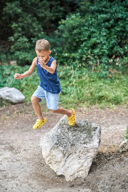istock Active little boy jumps down from large rock in green park 1470943695
