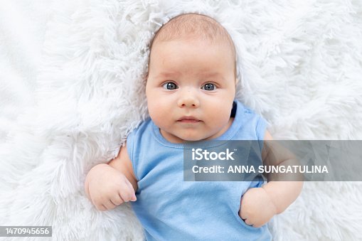 istock portrait of a cute baby boy three months old in a blue bodysuit on a white bed at home 1470945656