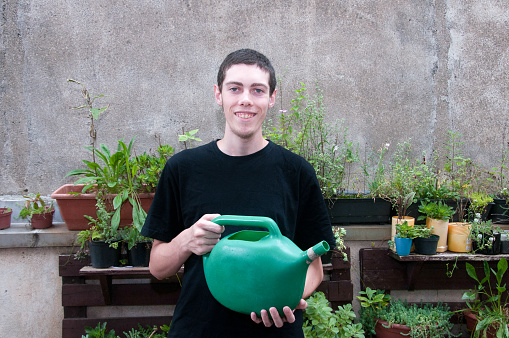 Young man watering plants in the garden with a big green watering can