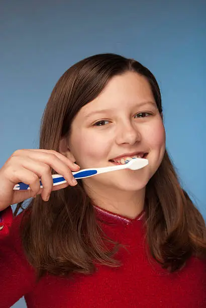 Little girl brushing her teeth.   Studio shot on blue background.