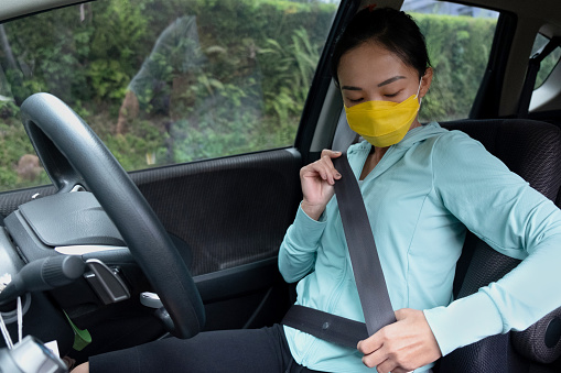 Side shot of Asian woman with face mask putting on seat belt before driving car