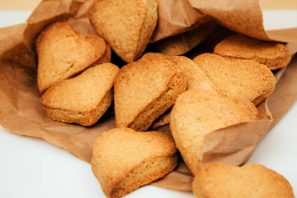 galletas de mantequilla en forma de corazones en una bolsa de papel marrón sobre una mesa blanca - natural form fotografías e imágenes de stock