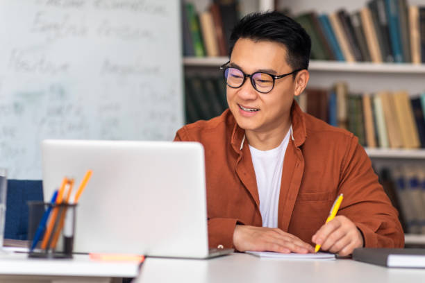 istock Japanese Male Tutor At Laptop Taking Notes Sitting At Workplace 1470958602