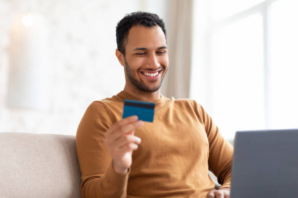 istock Smiling man using pc and credit card sitting on couch 1470959291
