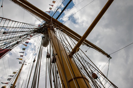 An array of multicolored ropes is seen tied to the masts of a vintage sailing vessel, rising up to the sky