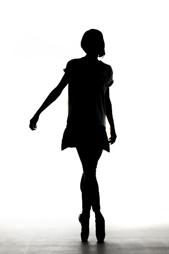 Silhouette of a ballerina wearing shirt and elegant dress standing against white background