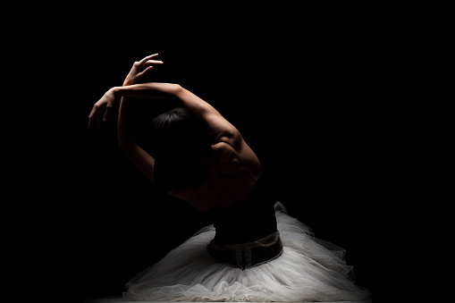 Half silhouette modern ballet dancer. Balerina posing on dark background