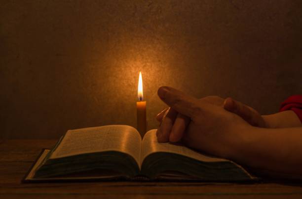 istock Person sitting in a cozy environment, reading a Bible with a lit candle 1470961547