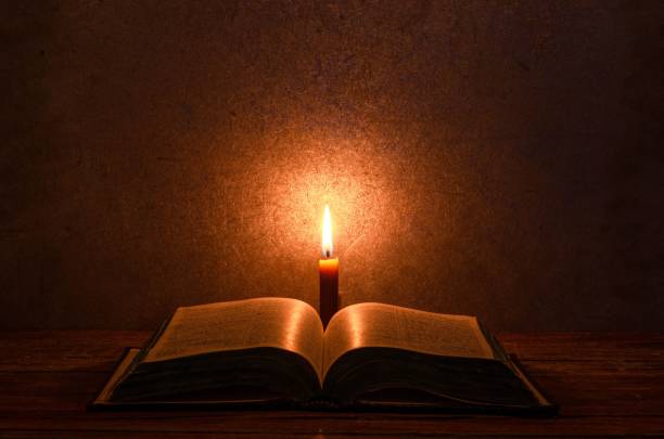 istock Wooden table with an open Bible book, illuminated by a single candle burning on top 1470961578