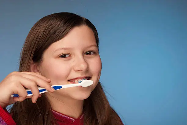 Little girl brushing her teeth.   Studio shot on blue background.