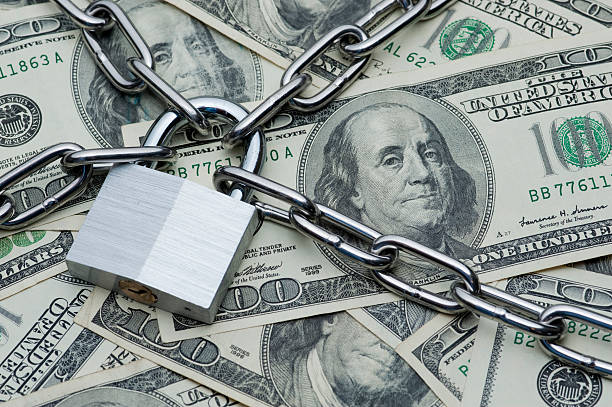 A lock and chain over a pile of hundred dollar bills stock photo