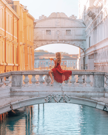 In this photo, a young woman wearing a stunning red dress is sitting on the Bridge of Sighs in St. Mark's Square in Venice, Italy. She is enjoying a delicious slice of pizza while taking in the beautiful views around her. The sun shines bright in the clear blue sky, casting a warm glow over the ancient bridge and the surrounding buildings.
The woman appears to be completely absorbed at the moment, savoring each bite of the mouth-watering pizza and soaking in the unique ambiance of Venezia Italia. Behind her, we can see the intricate architecture of the city's famous buildings and the shimmering waters of the canal below.
Overall, this photo captures a beautiful moment of relaxation and indulgence in one of the most picturesque and iconic locations in Venice.
