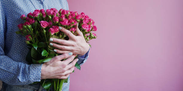 International Women's Day.Concept of greeting banner for international women's day on March 8.Close-up girl's hands holding large bouquet pink roses on pink background,copy space. Mother's day banner día internacional de la mujer.concepto de pancarta de saludo para el día internacional de la mujer el 8 de marzo.primer plano de las manos de la niña sosteniendo grandes rosas rosas rosas sobre fondo rosa, espacio de copia. banner del día de la madre.