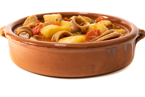 A potato stew with calamari, served in a clay bowl, isolated on a white background. Spanish food concept.
