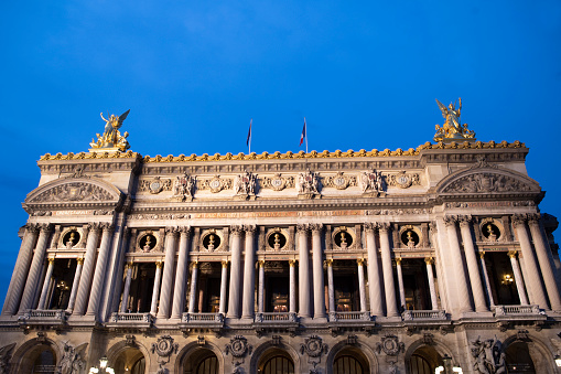 Paris, France – September 23rd, 2022: The Palais Garnier, also known as Opéra Garnier, is possibly the most famous opera house in the world - partly due to its use as the setting for the novel 'The Phantom of the Opera'. Photographed here early evening, shortly after being illuminated by floodlights from nearby apartment buildings.