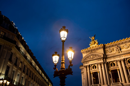 Paris, France – September 23rd, 2022: The Palais Garnier, also known as Opéra Garnier, is situated in the 9th arrondissement of Paris, France. Crowds of people wait at the end of the day to see the floodlights from the tops of surrounding apartments switch on to illuminate the magnificent building.